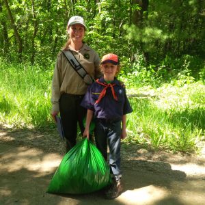 Bradlee Gehlhoff, a second-grader at St. Paul Lutheran School in Stevensville, shows off the bag filled with invasive garlic mustard plants he’d plucked at Grand Mere State Park this summer. The DNR’s Heidi Frei, left, said volunteers are a huge help in keeping invasive species under control. Photo Credit: Mary Gehlhoff