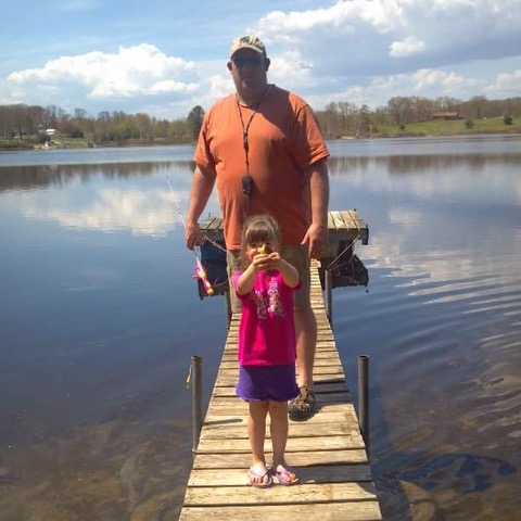 A little girl holding a fish in front of her dad