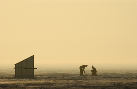 Two people standing on ice in the early morning hours preparing to go ice fishing